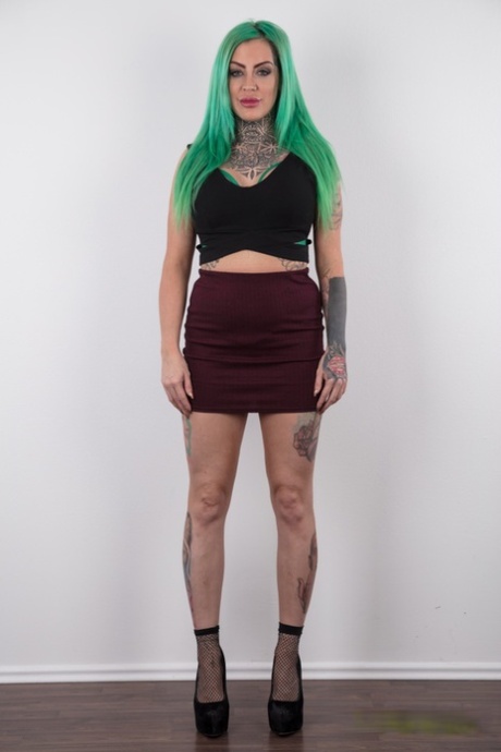 Tattooed girl with green hair and pierced nipples stands naked after disrobing