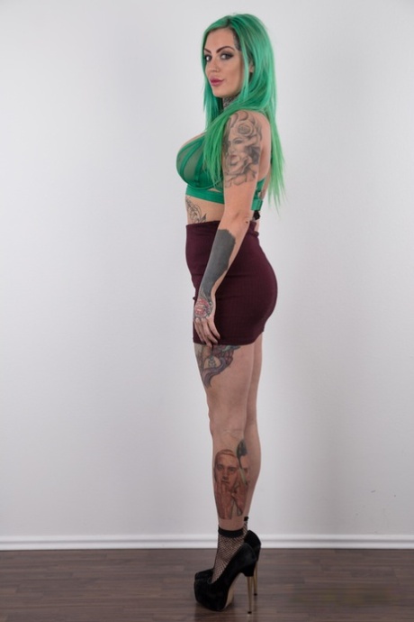 Tattooed girl with green hair and pierced nipples stands naked after disrobing