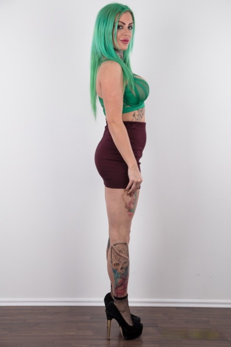 Tattooed girl with green hair and pierced nipples stands naked after disrobing