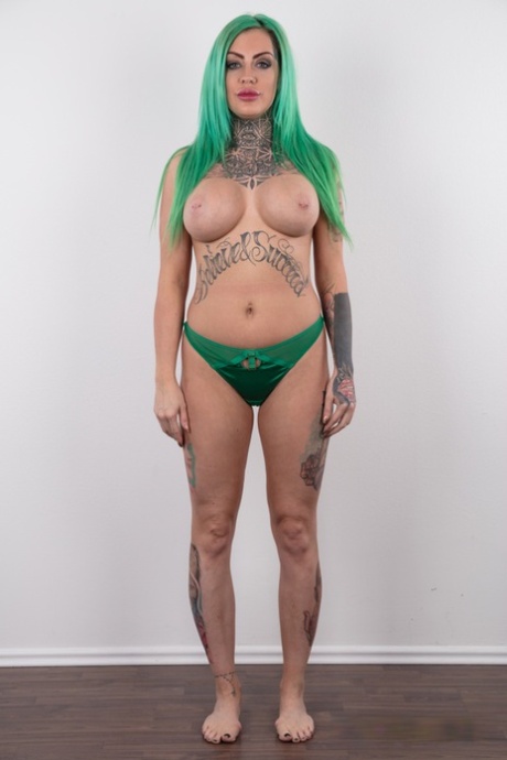 Tattooed girl with green hair and pierced nipples stands naked after disrobing