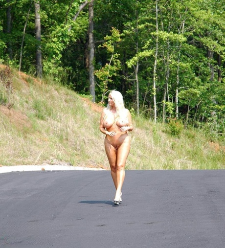 Busty blonde Karen Fisher wanders a paved road while naked before masturbating